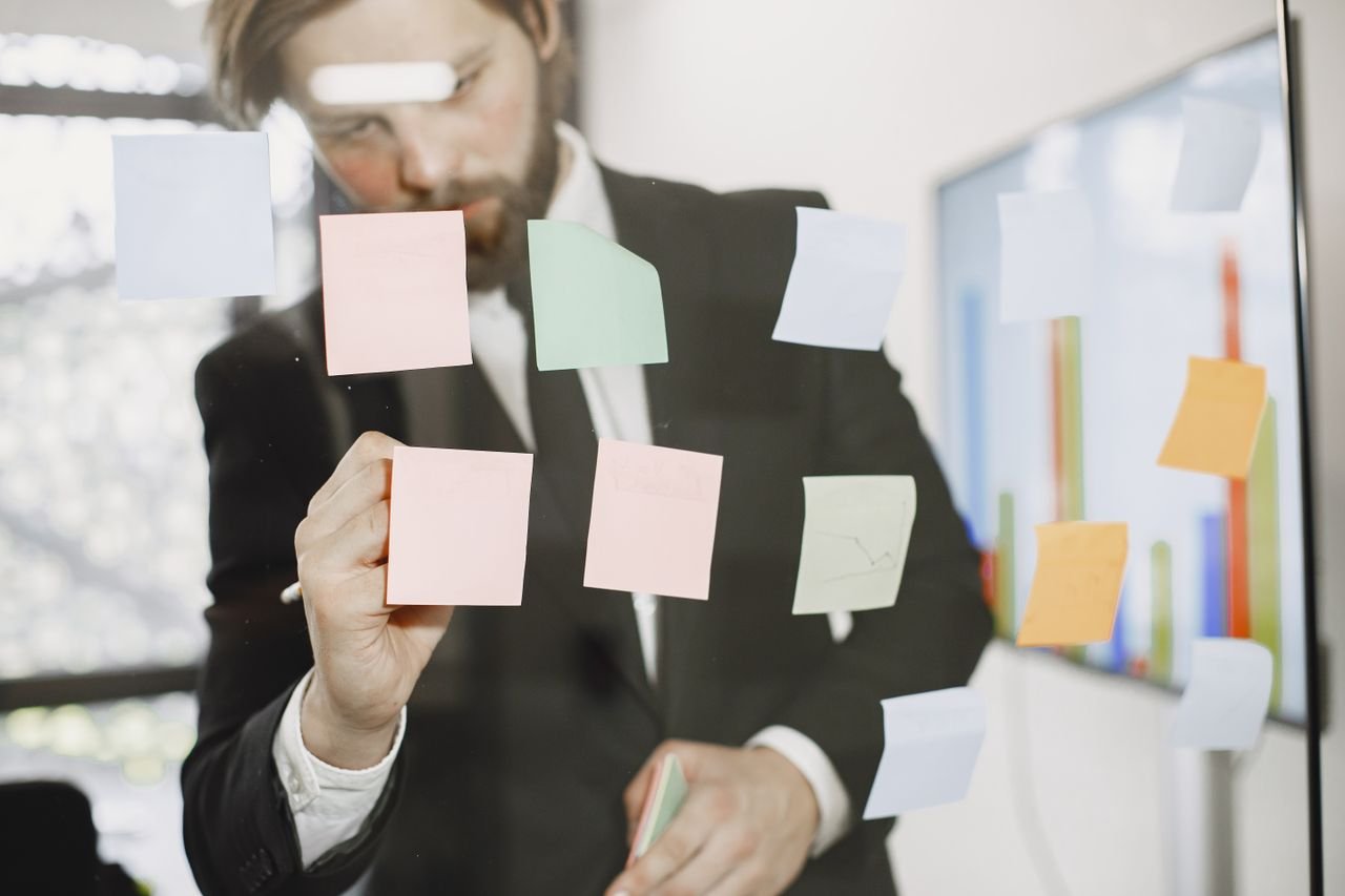 Professional man utilizes sticky notes on glass for planning in an office setting.